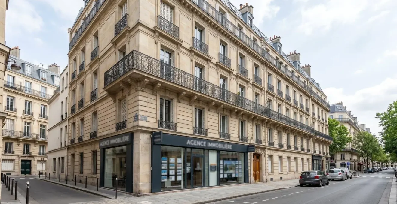 Façade d'immeuble haussmannien parisien typique avec agence immobilière au rez-de-chaussée, vitrine moderne, rue calme et lumineuse