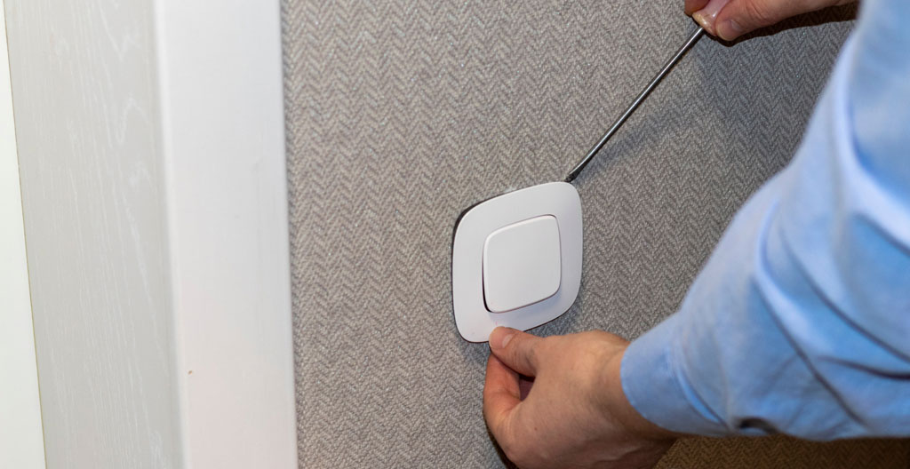 Gros plan d'une main inspectant une prise électrique sur un mur blanc dans un appartement en visite