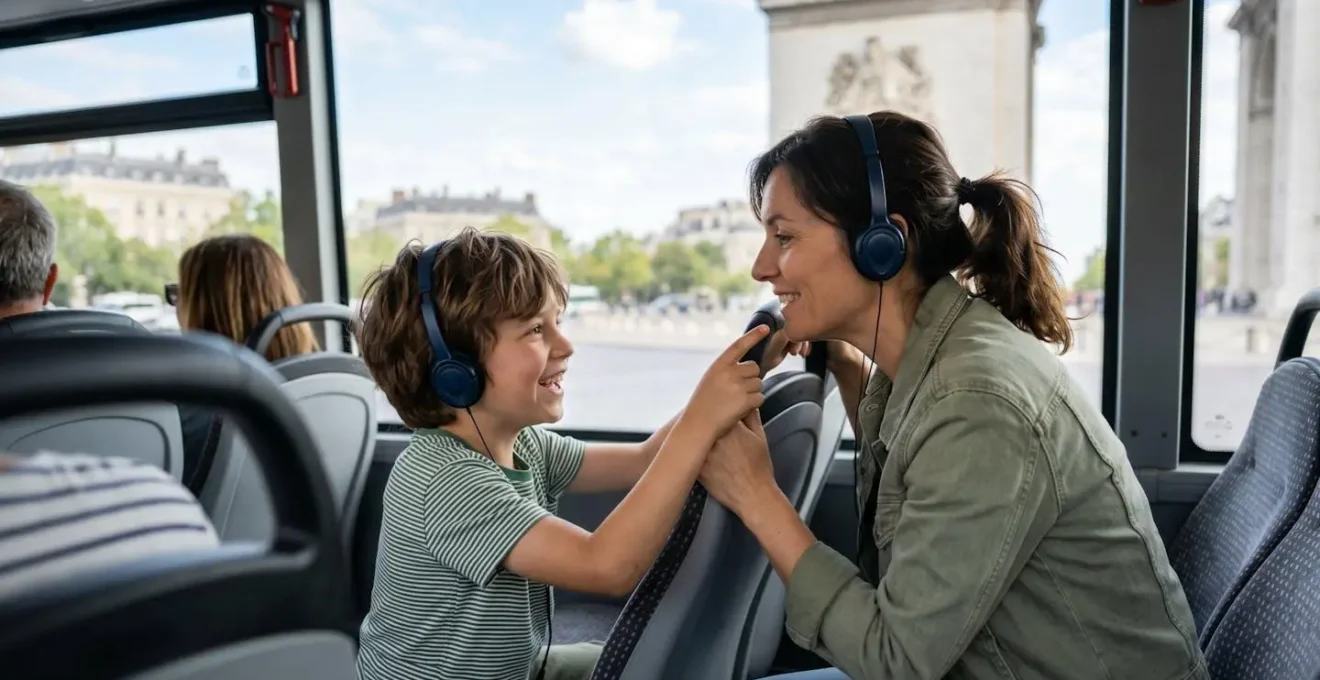 Vue de profil d'un parent et d'un enfant assis côte à côte dans un bus touristique, l'enfant pointant du doigt vers la fenêtre avec un sourire, tous deux portant des écouteurs audio-guide, monuments parisiens flous en arrière-plan